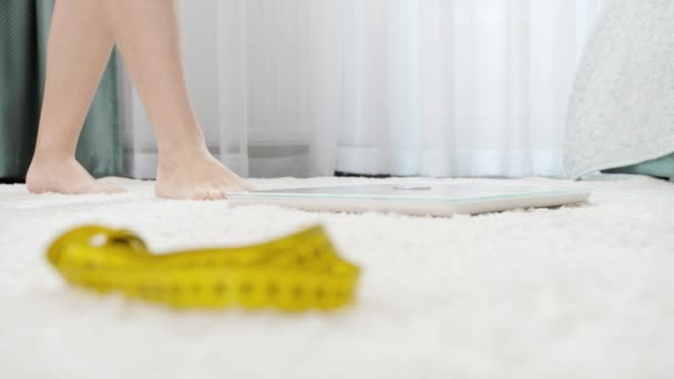 Camera focusing on measuring tape and woman weighting on scales at bedroom. Concept of dieting, loosing weight and healthy lifestyle. — Stock Video