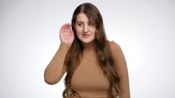 Studio portret van een lachende vrouw die hand in oor houdt en iemand hoort praten. Het begrip roddel, het verkrijgen van informatie en het luisteren naar geheimen — Stockvideo