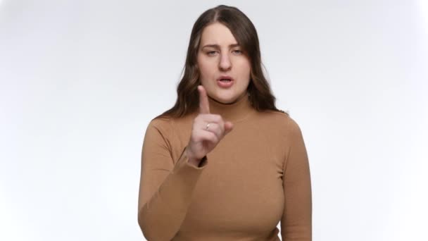 Studio portrait of young woman saying hush and putting finger at lips. Concept of keeping secret and silence — Stock Video