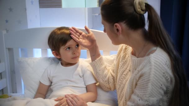 Mladá matka dotýká a líbá svého malého syna s vysokou teplotou na čele. Koncepce dětské nemoci, nemoci a rodičovské péče — Stock video