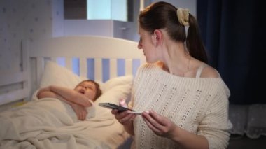 Diğer genç hasta oğlunun ateşini ölçüyor ve telefonla doktoru arıyor. Çocuk hastalığı, hastalık ve ebeveyn bakımı kavramı