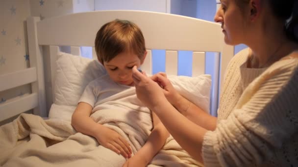 Giovane madre seduta accanto al figlio malato e misurare la temperatura corporea. Concetto di malattia dei bambini, malattia e cura dei genitori — Video Stock