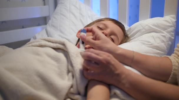 Fürsorgliche Mutter streichelt ihren kleinen kranken Sohn, der im Bett die Temperatur misst. Konzept der Kinderkrankheit und der elterlichen Betreuung — Stockvideo