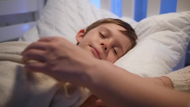 Schattig jongetje dat slaapt terwijl moeder hem kust en de deken aanpast. Begrip ouderschap en gezinsgeluk. — Stockvideo