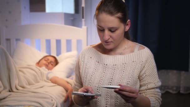 Young woman sitting next to bed of her sick son feeling unwell and talking to doctor. Concept of children illness, disease and parent care — Stock Video