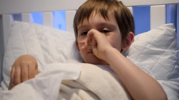 Retrato de un niño enfermo con secreción nasal acostado en la cama y sonándose la nariz en papel. Concepto de enfermedad infantil, enfermedad y atención sanitaria — Vídeo de stock