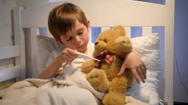 Portrait of cute sick boy measuring temperature to his toy teddy bear with digital thermometer. Concept of child virus and kids protection during coronavirus Covid-19 pandemic. — Stock Video