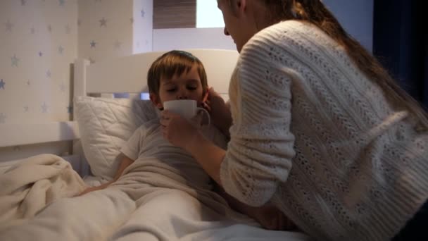 Mãe carinhosa medindo a temperatura para seu pequeno filho doente e dando-lhe chá quente na caneca. Conceito de doença infantil, doença. cuidados aos pais e tratamento doméstico. — Vídeo de Stock