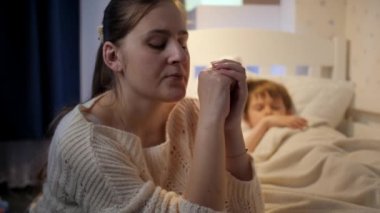 Depresyon ve kötü düşüncelerden muzdarip uyuyan oğlunun yanında oturan genç anne. Yalnız anne kavramı, aile sorunları ve annelik depresyonu.