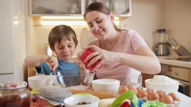 Mutlu gülümseyen çocuk evde pasta ya da pasta pişirirken annesini kaşıkla besliyor. Çocuklar aileleriyle yemek pişirir, küçük aşçı olur, aile birlikte vakit geçirir, ev mutfağı olur..