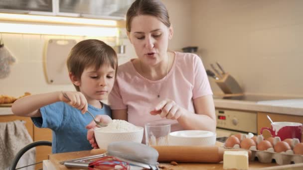 어린 소년 이 비스킷 반죽을 만들기 위해 유리잔에 밀가루를 부었습니다. 부모와 함께 요리하는 자녀들, 작은 요리사, 가족 이 함께 시간을 보내는 가정 주방. — 비디오