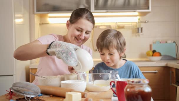 SMiling mother with little son pouring eggs in flour and mixing dough for pie or cake. Children cooking with parents, little chef, family having time together, domestic kitchen. — Stock Video