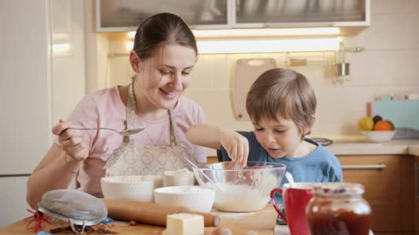 Glimlachend jongetje met moeder die ingrediënten mengt in een grote kom om deeg of biscuit te maken. Kinderen koken met ouders, kleine chef-kok, familie hebben tijd samen, huishoudelijke keuken. — Stockvideo