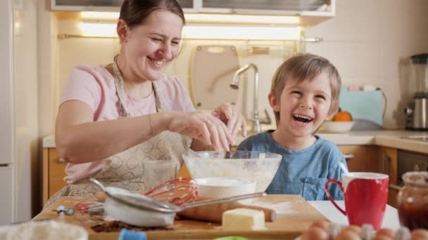 Glücklich lachender Junge mit Mutter, die spielt und herumalbert, während sie zu Hause Teig für Kekse backt. Kinder kochen mit Eltern, kleiner Koch, gemeinsame Zeit mit der Familie, häusliche Küche. — Stockvideo