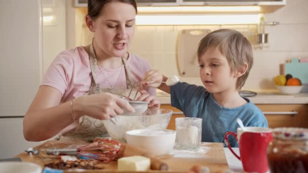 ふるいにかけ、生地を作るために小麦粉を注ぐ小さな男の子.両親、小さなシェフ、家族と一緒に時間を過ごす子供たち、家庭用キッチン. — ストック動画