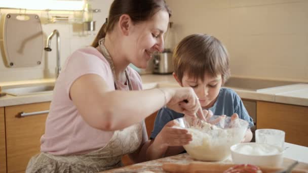 Αγοράκι που κάθεται με τη μητέρα του στην κουζίνα και ανακατεύει ζύμη για κέικ ή πίτα. Παιδιά μαγείρεμα με τους γονείς, λίγο σεφ, οικογένεια έχοντας χρόνο μαζί, οικιακή κουζίνα. — Αρχείο Βίντεο
