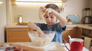 Küçük tatlı çocuk hamur yoğuruyor ve büyük cam kasede malzemeleri karıştırıyor.