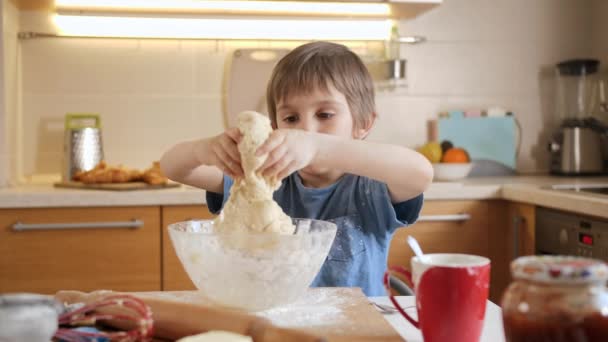 Bonito menino brincando e se divertindo com massa macia para biscoitos na cozinha. — Vídeo de Stock