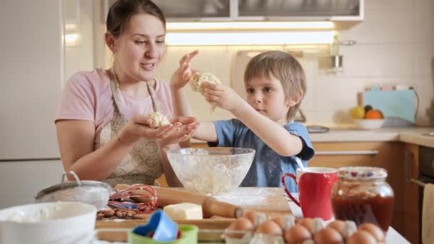 Ung mor med liten son knåda deg och bilda den för att rulla på träskiva. Barn matlagning med föräldrar, liten kock, familj har tid tillsammans, kök. — Stockvideo