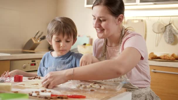 Feliz niño sonriente con la madre haciendo galletas y poniéndolas en forma de hornear. Niños cocinando con padres, pequeño chef, familia pasando tiempo juntos, cocina doméstica. — Vídeos de Stock