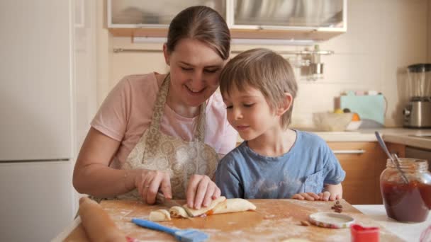 Kisfiú nézi anya vágás keksz vagy édes tekercs lekvártöltelékkel. Gyerekek főzés a szülőkkel, kis szakács, családi együttlét, háztartási konyha. — Stock videók