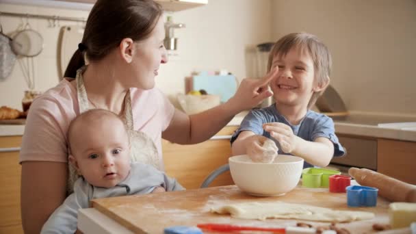 料理をしながら楽しそうにキッチンで遊んでいる子供たちと幸せな母親。両親、小さなシェフ、家族と一緒に時間を過ごす子供たち、家庭用キッチン. — ストック動画