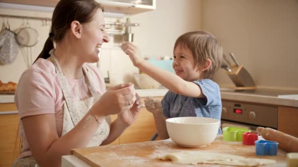 Glad skrattande pojke med att leka med mamma medan matlagning och kasta mjöl. Barn matlagning med föräldrar, liten kock, familj har tid tillsammans, kök. — Stockvideo