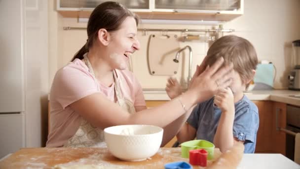 Mère riante avec son fils se jetant de la farine tout en cuisinant à la maison. Cuisine des enfants avec les parents, petit chef, famille ayant du temps ensemble, cuisine domestique. — Video