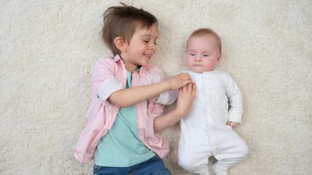 아기 동생 과 함께 카펫 위에 누워 재미있게 웃고 있는 행복 한 소년. 자녀들의 행복 과 가족 관계. — 비디오