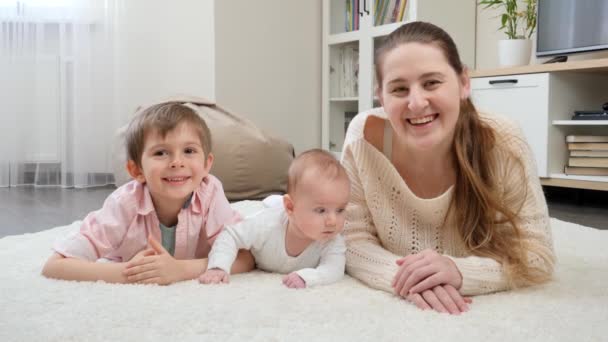 거실에 있는 큰 카펫 위에 누워 미소짓고 카메라로 웃는 행복 한 가족. 부모, 자녀 의행 복 및 가족 관계 — 비디오
