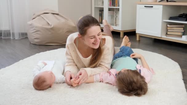 Bébé mignon et garçon plus âgé couché avec une mère souriante sur le tapis dans le salon. Parentalité, bonheur des enfants et relation familiale — Video