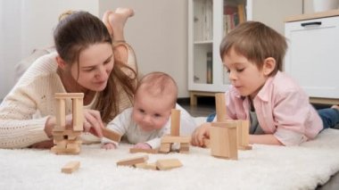 Genç anne, küçük oğullarıyla oturma odasında halının üzerinde oynuyor. Ebeveynlik, çocuklar mutluluk ve aile ilişkileri ve eğitim.