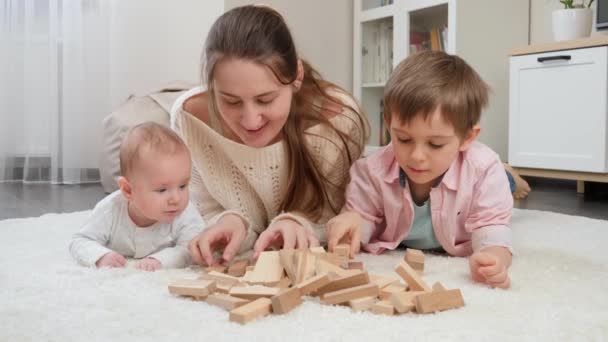 Mulher sorridente deitada no chão com menino e filho mais velho e brincando com blocos de brinquedo de madeira. Paternidade, felicidade das crianças e relacionamento familiar — Vídeo de Stock