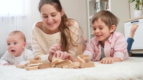 Glücklich lächelnde Familie, die zu Hause mit Holzklötzen auf Teppich spielt. Elternschaft, Kinderglück und Familienbeziehung — Stockvideo