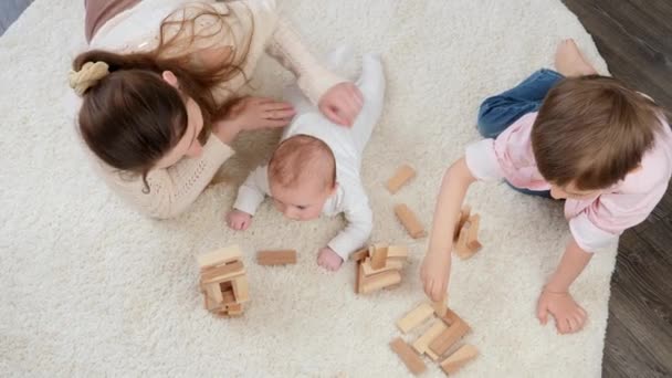 Top kilátás anya a baba és az idősebb fiú játszik szőnyegen játék fa blokkok. Szülői, gyermeki boldogság és családi kapcsolat — Stock videók