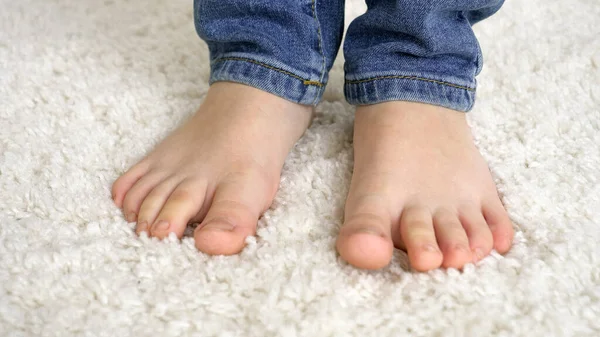 Pequeño chico descalzo en jeans caminando sobre una suave alfombra blanca en casa —  Fotos de Stock