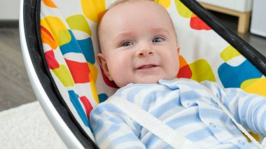 Elektrikli sallanan koltukta gevşeyen mavi gözlü gülümseyen erkek bebek portresi. Çocuk gelişimi ve mutlu çocukluk