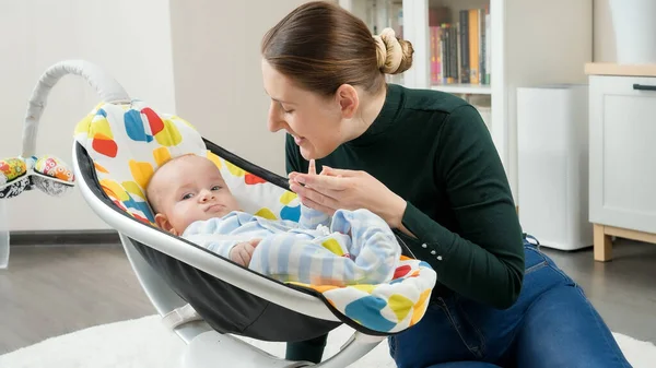 Retrato de mãe sorridente sentada ao lado do filhinho balançando na cadeira elétrica. Desenvolvimento infantil e paternidade feliz — Fotografia de Stock