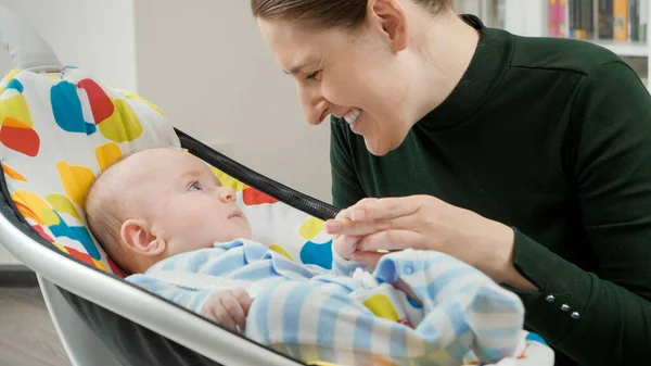 Retrato de una madre sonriente mirando a su lindo hijo sentado en una mecedora eléctrica. Desarrollo infantil y crianza feliz — Foto de Stock