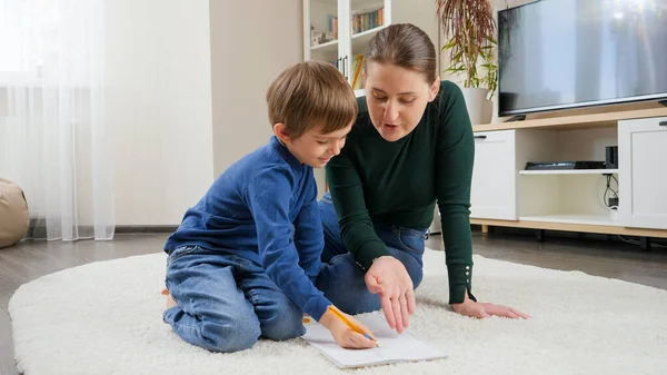 年轻的母亲在客厅的地板上训斥和喊她的儿子做作业。家庭教育、儿童发展和养育子女问题的概念 — 图库照片
