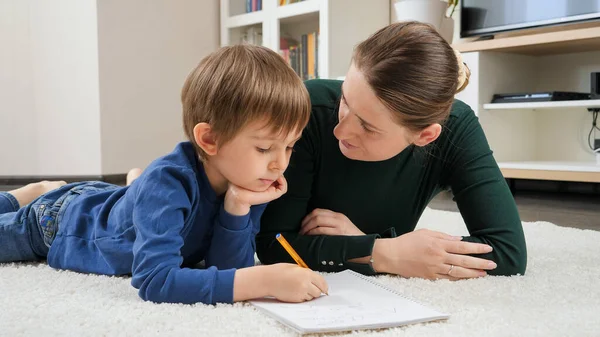 Mère en colère gronder et parler à son fils stupide faire des devoirs sur le sol dans le salon. Concept d'éducation domestique, de développement de l'enfant et de problèmes parentaux — Photo