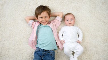Ağabeyi halının üzerinde yatıp kameraya gülümseyen tatlı bir erkek bebek. Çocukların mutluluğu ve aile ilişkileri