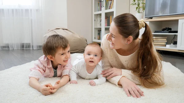 Lindos niños pequeños acostados con madre joven en la alfombra en la sala de estar. Crianza, felicidad de los hijos y relación familiar. — Foto de Stock