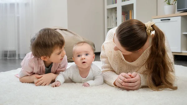 Szczęśliwa uśmiechnięta rodzina leżąca na dużym dywanie w salonie i uśmiechnięta przed kamerą. Rodzicielstwo, szczęście dzieci i relacje rodzinne — Zdjęcie stockowe