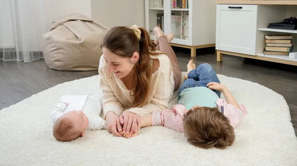 Bébé mignon et garçon plus âgé couché avec une mère souriante sur le tapis dans le salon. Parentalité, bonheur des enfants et relation familiale — Photo