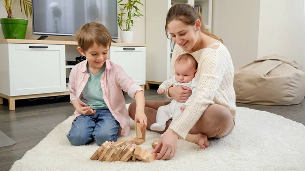 Счастливая мать с маленькими сыновьями, играющими в игры на полу в гостиной. Родители, дети счастье и семейные отношения — стоковое фото