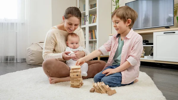 Молодая мать держит мальчика и играет со своим старшим сыном в деревянных блоках. Родители, дети счастье и семейные отношения — стоковое фото