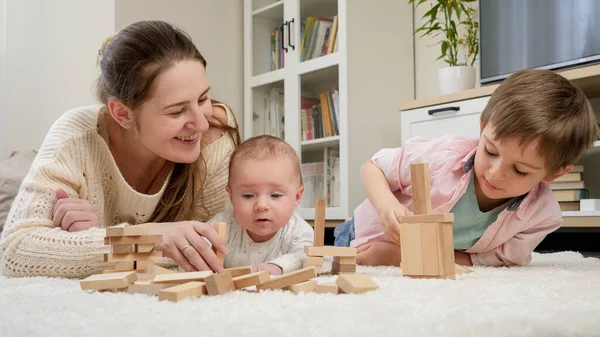 Милый мальчик лежит со своей семьей на ковре и играет с игрушечными деревянными блоками. Родители, дети счастье и семейные отношения — стоковое фото