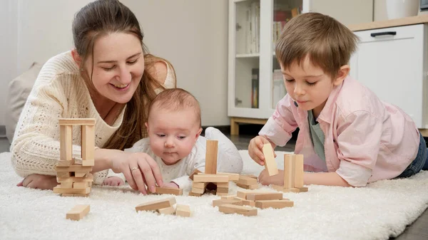 Jonge moeder speelt met haar zoontjes op tapijt in de woonkamer. Ouderschap, geluk van kinderen en familierelatie en onderwijs. — Stockfoto