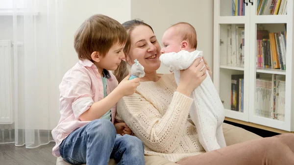 Niño pequeño con la madre jugando con el hermano bebé recién nacido y juguete sonajero. Crianza, felicidad de los hijos y relación familiar — Foto de Stock